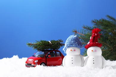 Photo of Cute decorative snowmen and toy car with fir tree branches on artificial snow against light blue background, space for text
