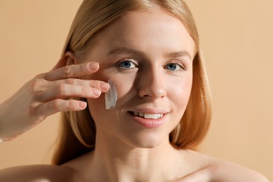 Beautiful young woman with sun protection cream on her face against beige background