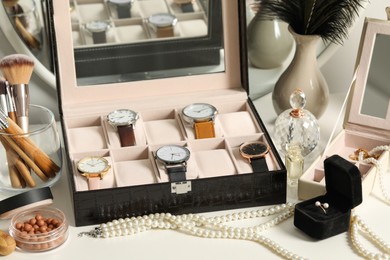 Photo of Jewelry boxes with many stylish wristwatches, accessories, perfumes, makeup brushes and decor on white table