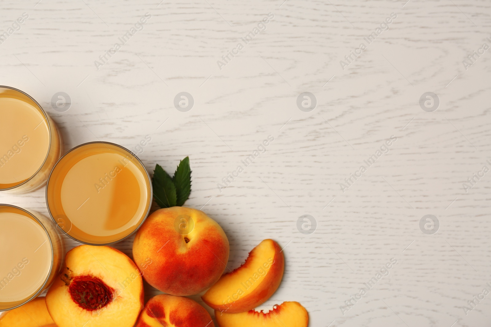 Photo of Glasses of delicious peach juice and fresh fruits on white wooden table, flat lay. Space for text