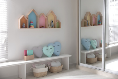 Cute children's room interior design with house shaped shelves on white wall and bench