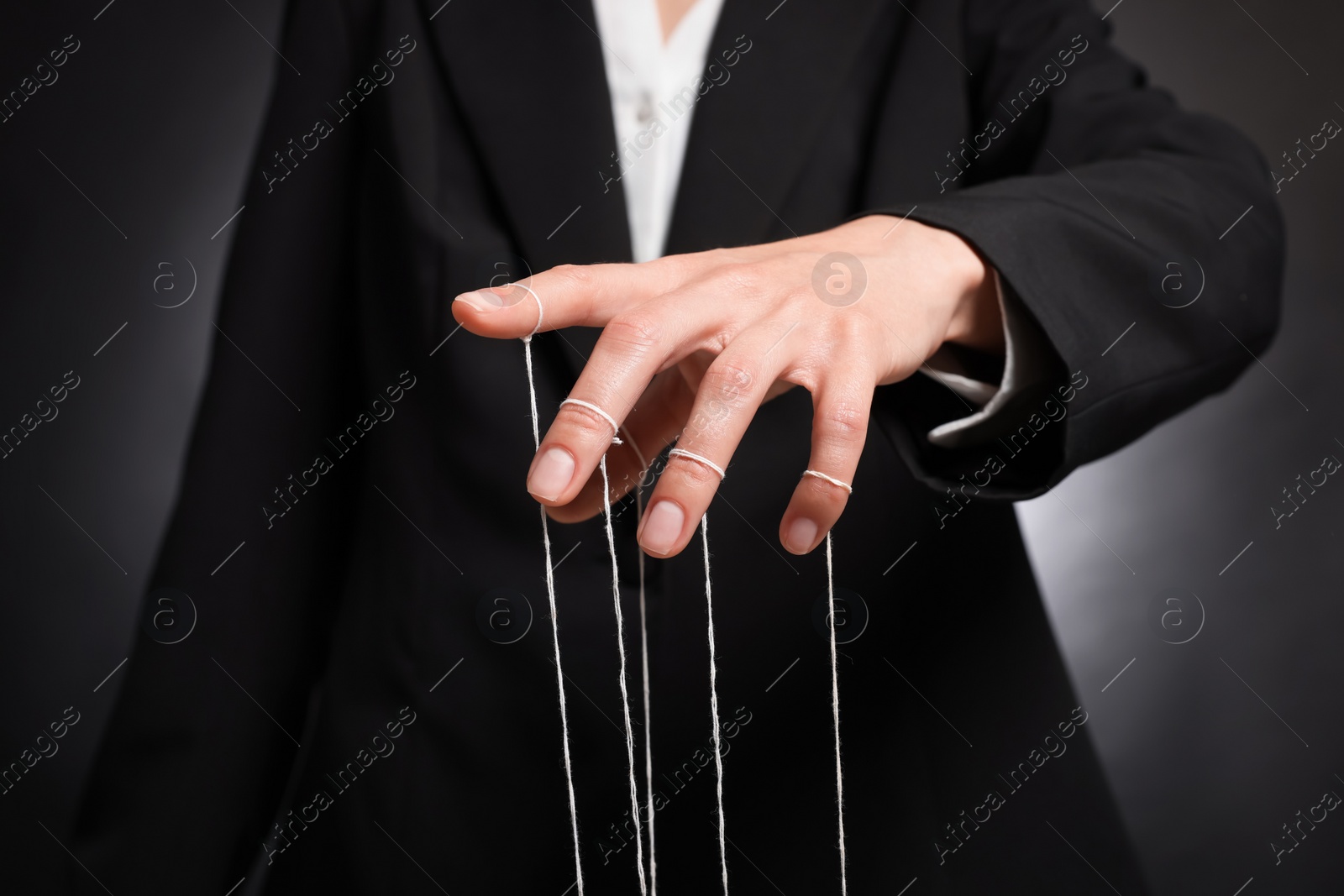 Photo of Woman in suit pulling strings of puppet on dark background, closeup