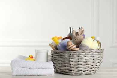 Photo of Wicker basket with different baby cosmetic products, accessories and toys on white wooden table