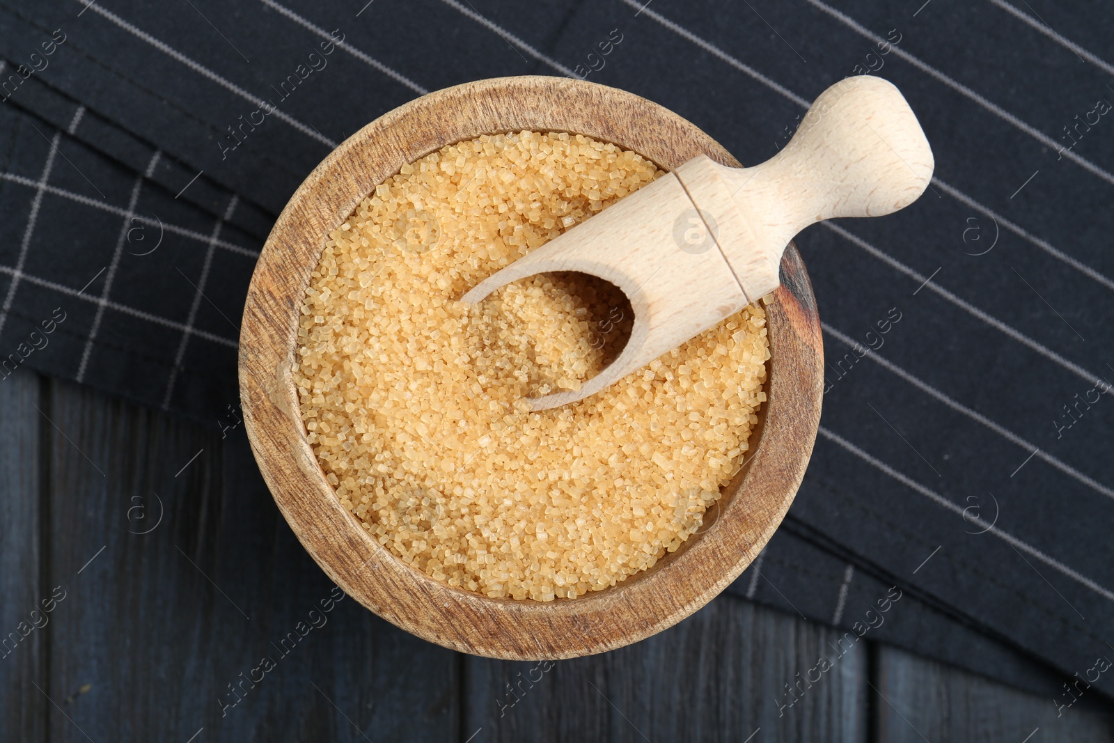 Photo of Brown sugar in bowl and scoop on black wooden table, top view