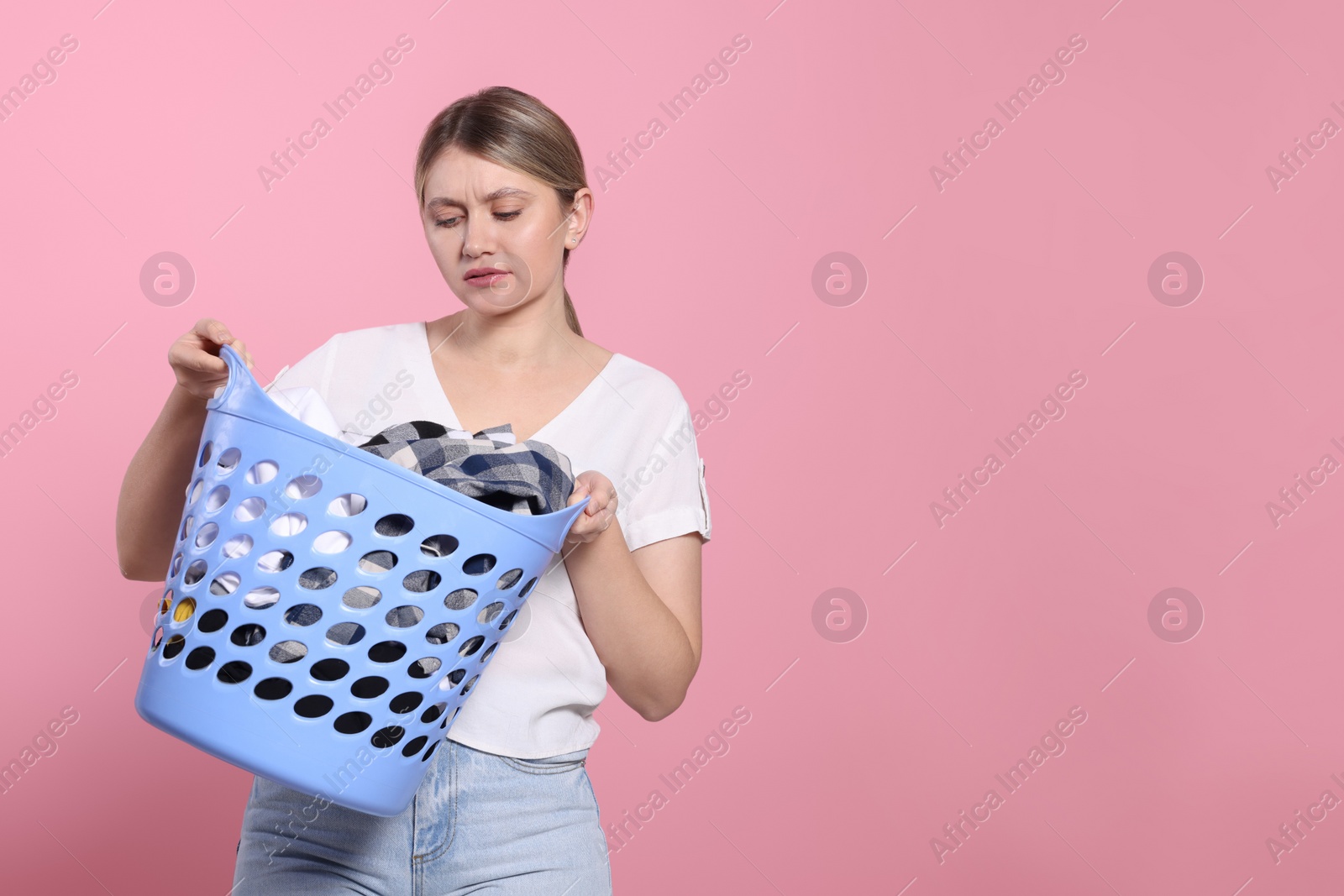 Photo of Young woman with basket full of laundry on pink background. Space for text