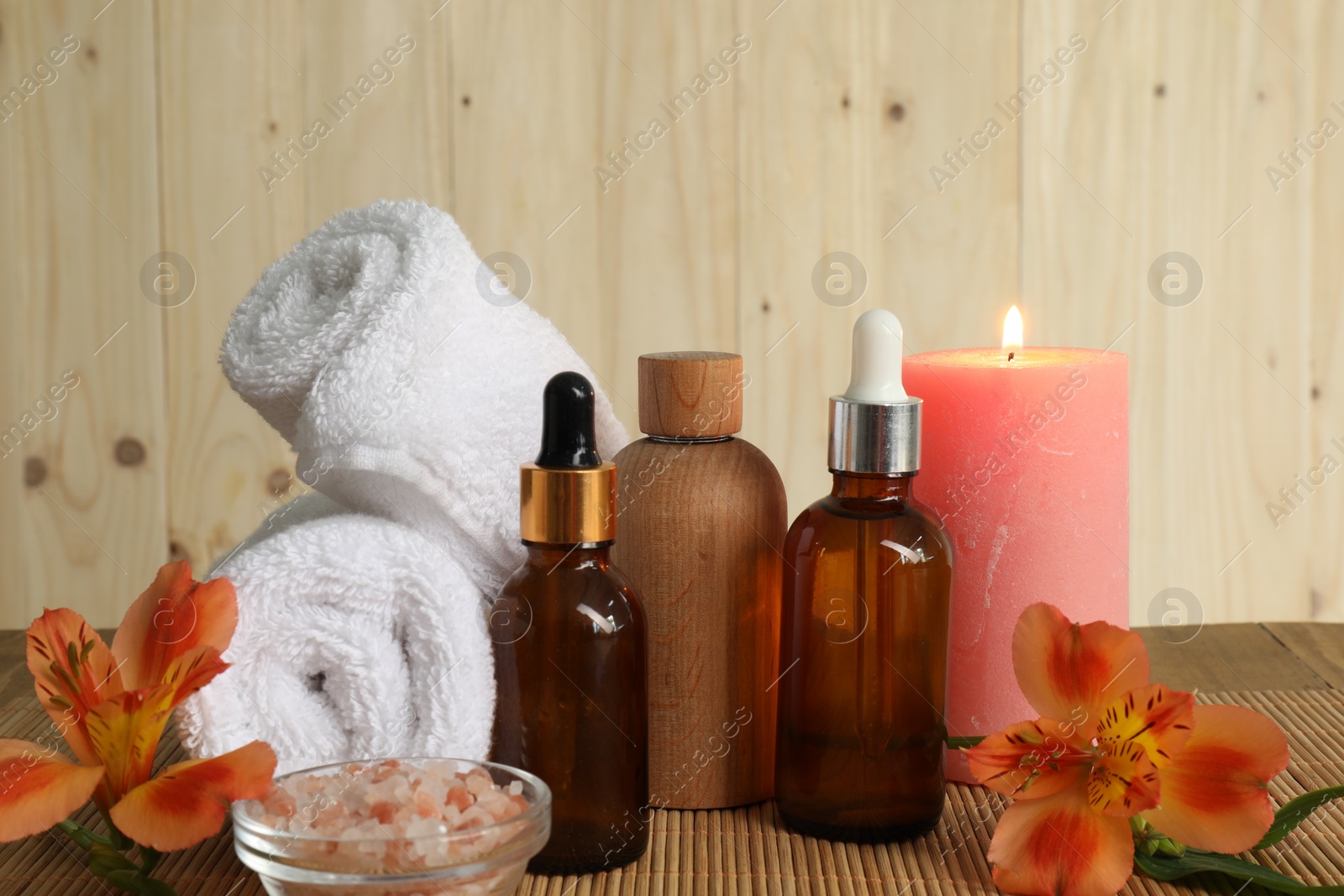 Photo of Aromatherapy. Essential oil in bottles, candle, sea salt, flowers and towel on bamboo mat, closeup