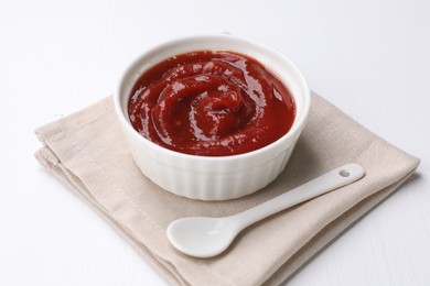 Photo of Organic ketchup in bowl and spoon on white table. Tomato sauce