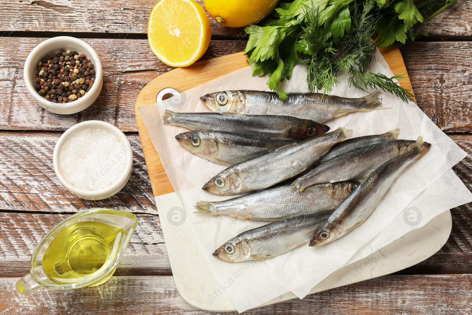 Photo of Fresh raw sprats and products on wooden table, flat lay