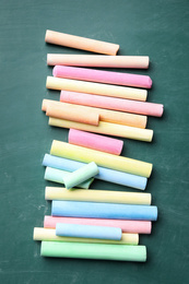 Photo of Pieces of color chalk on greenboard, flat lay