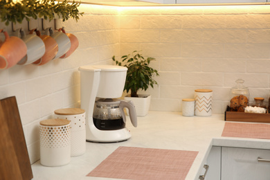 Modern coffeemaker on countertop near brick wall in kitchen