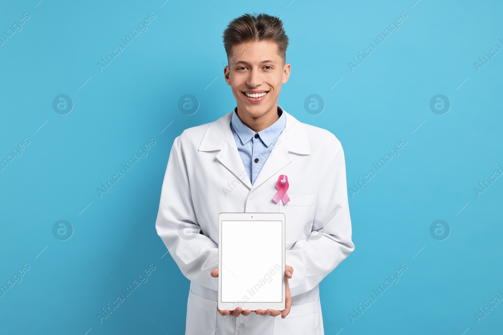 Photo of Mammologist with pink ribbon showing tablet on light blue background. Breast cancer awareness