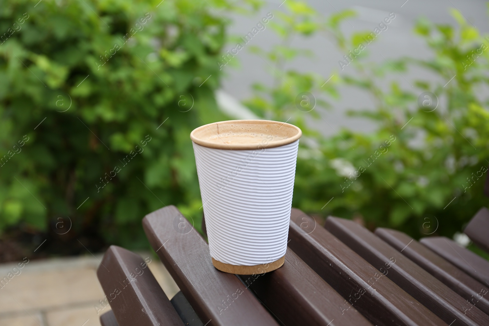 Photo of Paper cup of coffee on wooden bench outdoors. Takeaway drink