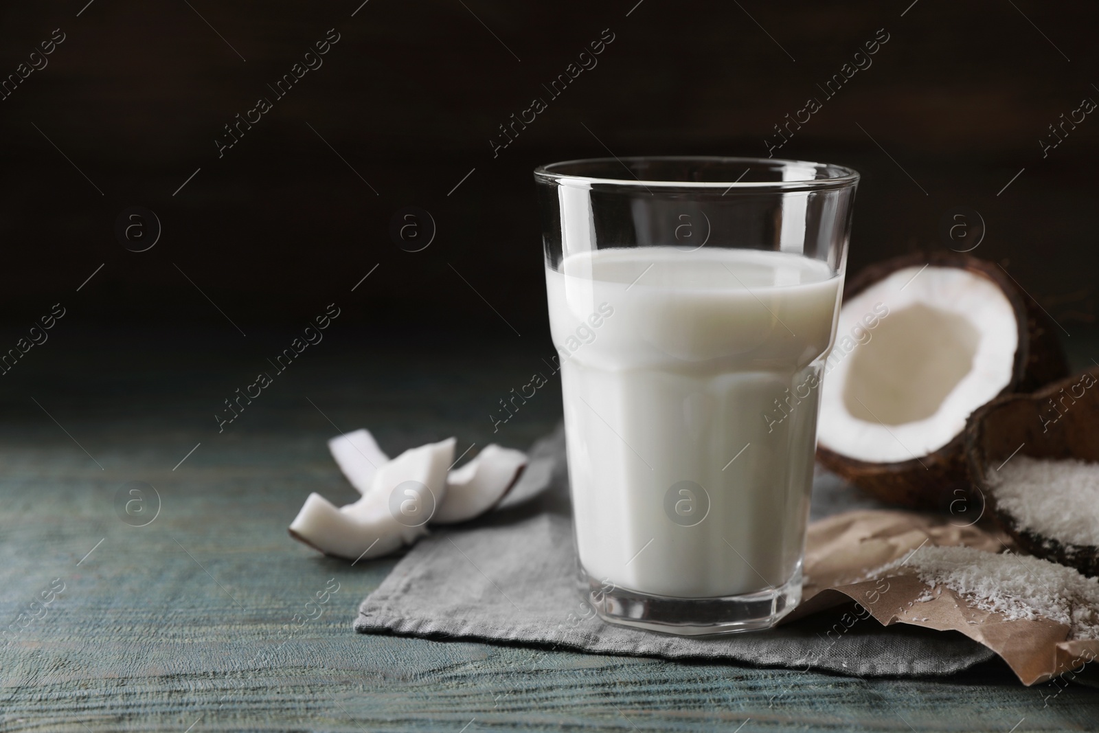 Photo of Glass of coconut milk, flakes and nut pieces on wooden table, space for text