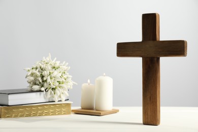 Photo of Burning church candles, wooden cross, ecclesiastical books and flowers on white table