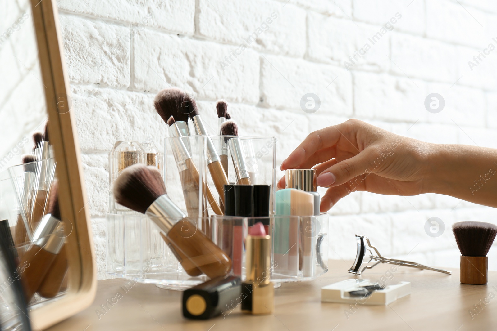 Photo of Woman taking cosmetics from organizer for makeup products on table