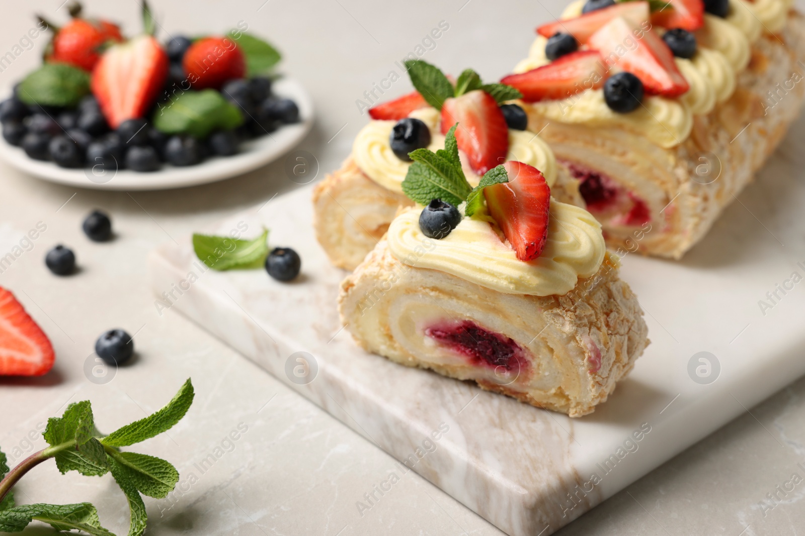 Photo of Tasty meringue roll with jam, cream, strawberry, blueberry and mint on light grey table, closeup