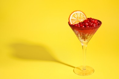 Photo of Martini glass with cranberries and dry orange slice on yellow background. Space for text