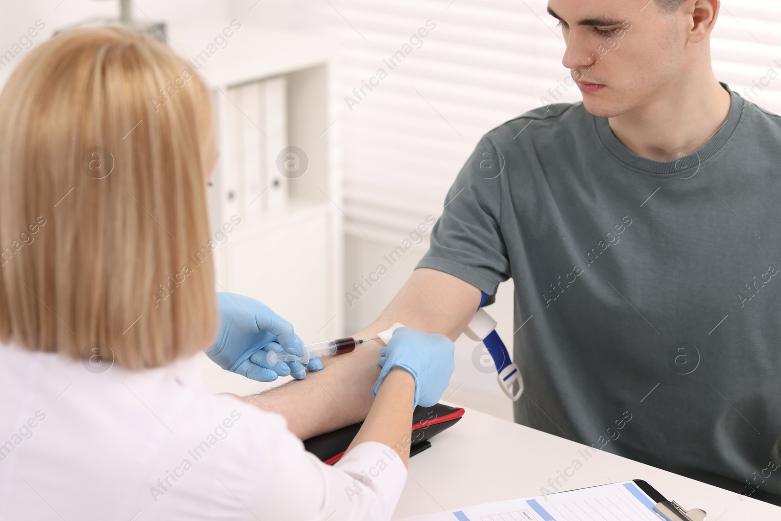 Photo of Doctor taking blood sample from patient with syringe at white table in hospital