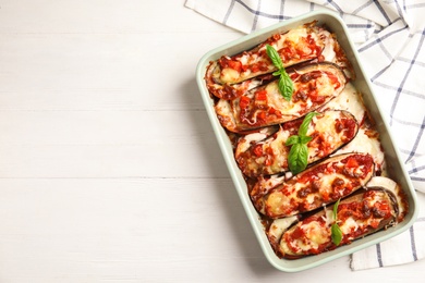 Photo of Baked eggplant with tomatoes, cheese and basil in dishware on white wooden table, flat lay. Space for text