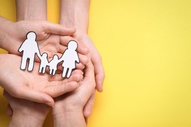 People holding paper family cutout on yellow background, top view. Space for text