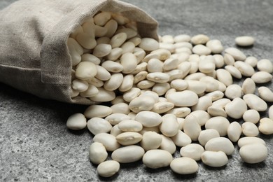 Photo of Bag with raw white beans on grey table, closeup