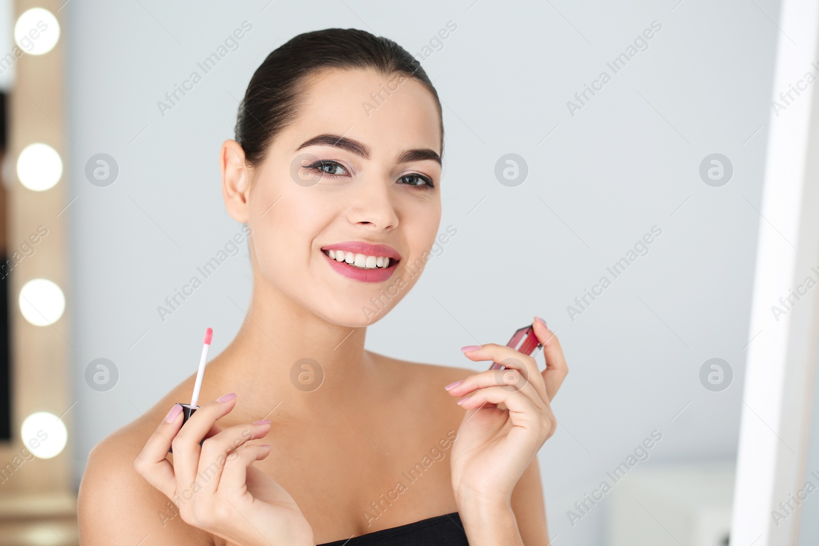 Photo of Young woman applying liquid lipstick on blurred background. Space for text