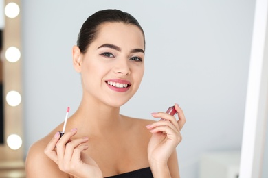 Young woman applying liquid lipstick on blurred background. Space for text