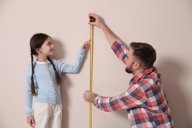 Photo of Father measuring daughter's height near beige wall