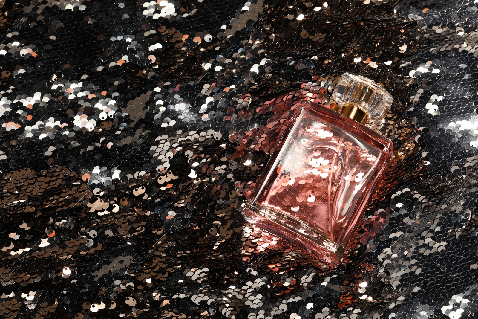 Photo of Luxury perfume in bottle on fabric with silver sequins, top view