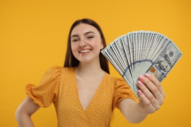 Happy woman with dollar banknotes on orange background, selective focus