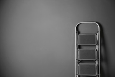 Photo of Modern metal stepladder against grey background. Space for text