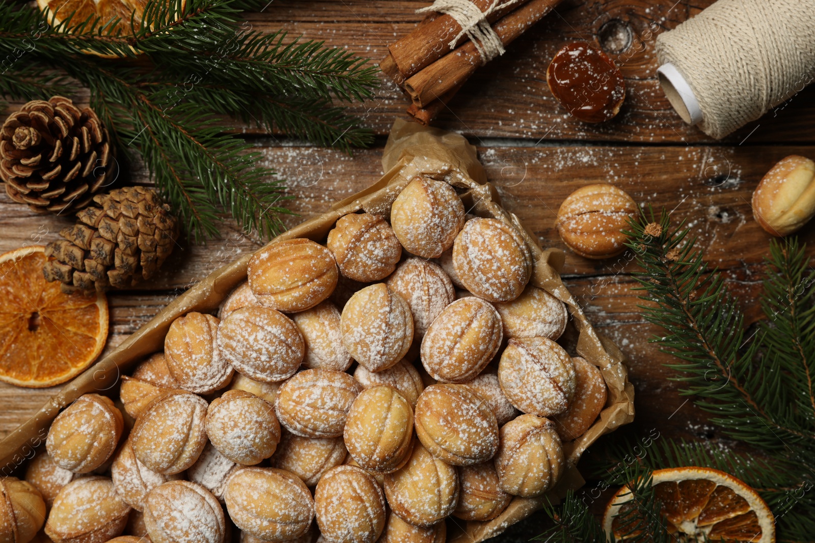 Photo of Delicious nut shaped cookies with boiled condensed milk, dry orange slices and fir tree branches on wooden table, flat lay