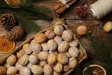 Delicious nut shaped cookies with boiled condensed milk, dry orange slices and fir tree branches on wooden table, flat lay