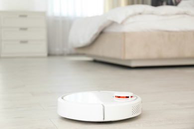Photo of Modern robotic vacuum cleaner on floor in bedroom. Space for text