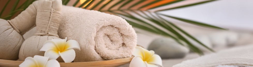 Image of Beautiful herbal bags, towel and plumeria flowers on massage table in spa cabinet, closeup. Banner design with space for text
