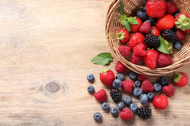 Wicker basket with many different fresh ripe berries on wooden table, flat lay. Space for text