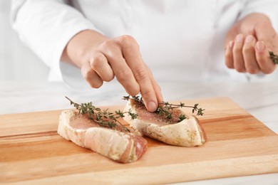 Photo of Professional chef decorating delicious meat with thyme at white table, closeup
