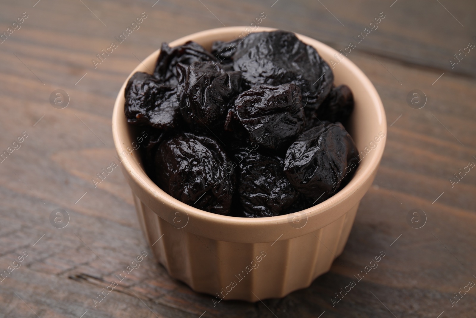 Photo of Sweet dried prunes in bowl on wooden table, closeup