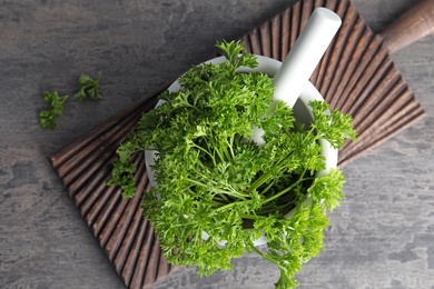 Mortar with fresh green parsley on grey background, top view