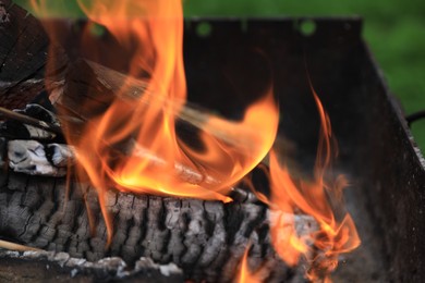 Photo of Metal brazier with burning firewood outdoors, closeup. Space or text