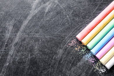 Pieces of color chalk on blackboard, flat lay. Space for text