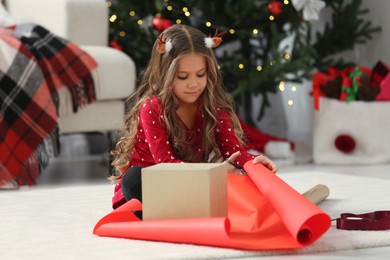 Photo of Cute little girl packing Christmas gift at home