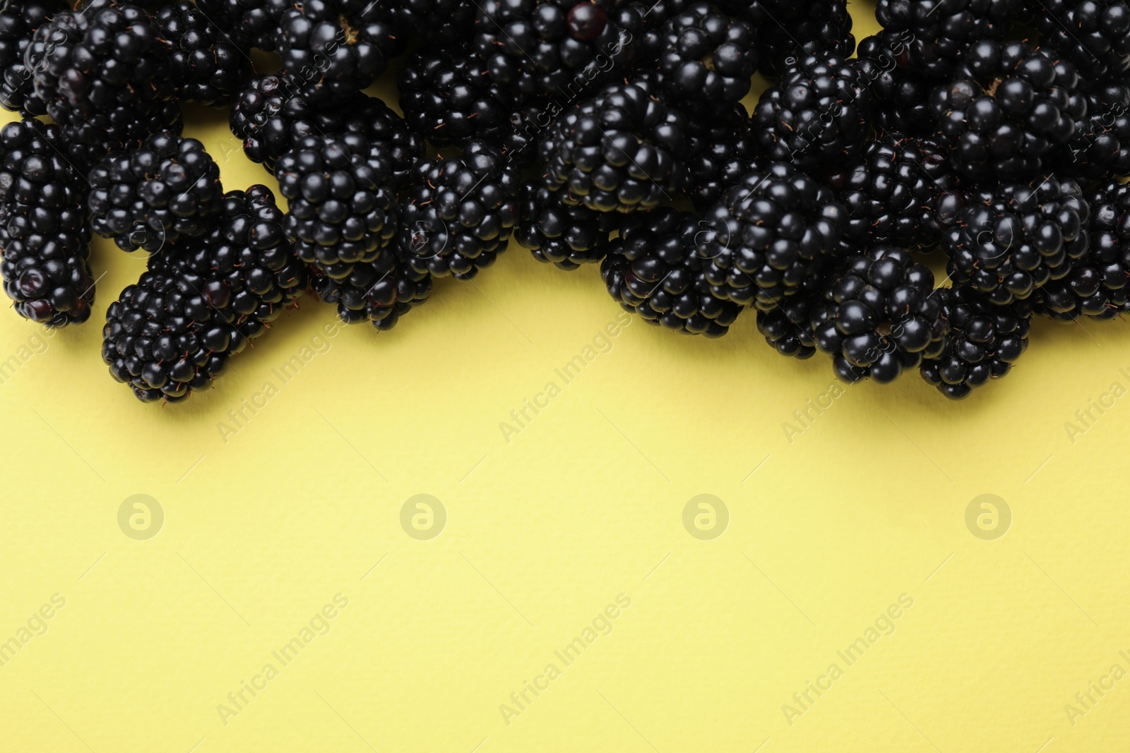 Photo of Tasty ripe blackberries on yellow background, flat lay. Space for text