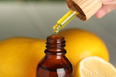 Photo of Woman dripping essential oil into bottle and lemons, closeup