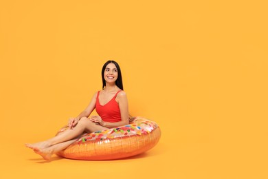 Happy young woman with beautiful suntan sitting on inflatable ring against orange background, space for text
