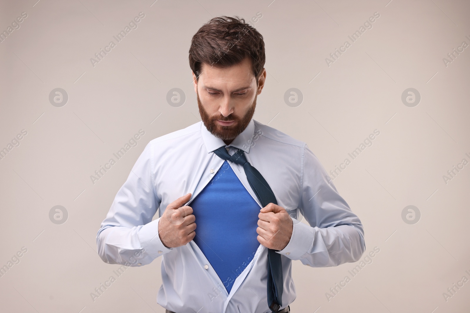 Photo of Confident businessman wearing superhero costume under suit on beige background