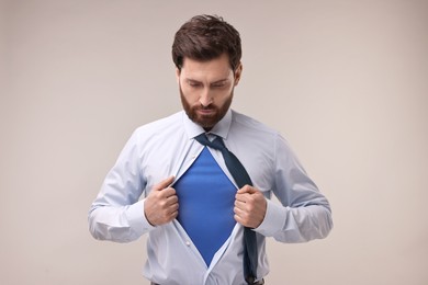 Confident businessman wearing superhero costume under suit on beige background