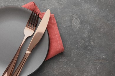 Photo of Clean plate, cutlery and napkin on grey textured table, top view. Space for text