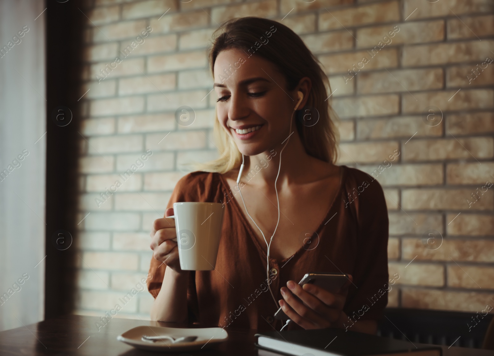 Photo of Woman with smartphone listening to audiobook at table in cafe