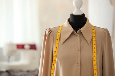 Photo of Mannequin with shirt and measuring tape in tailor shop, space for text